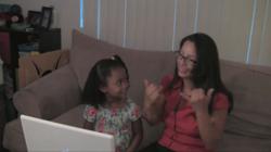 Photo of a A Deaf mother and her hearing daughter signing about a video they are watching.