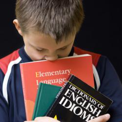 A young school boy carrying a number of English Language books. His nose is buried in them, in a frustrated fashion.