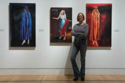 Susan Kraft stands near three pieces of her LET THEM EAT CAKE series in the Splintered Humanity Triton Museum of Art show in Santa Clara, CA