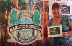 Rhonda Salisbury with the Yosemite Sierra Visitors Bureau shows the Best Idea Award from the Western Associatio of Convention and Visitors Bureau's alongside a display screen for the Majestic Mountain Loop, the idea that won the distinction.