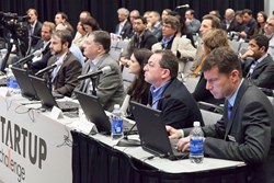Judges evaluate pitches from aspiring photonics entrepreneurs during the 2013SPIE Startup Challenge, as audience members look on.