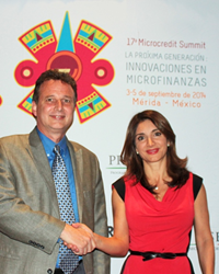Larry and Elenitza shaking hands in front of a backdrop printed with 17th Microcredit Summit logo