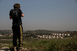 Palestinian child from the West Bank village of Nabi Saleh looks off at the Israeli settlement of Halamish.