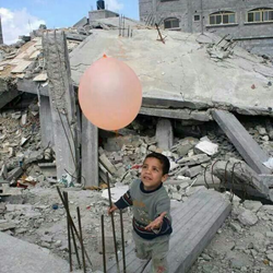 A young boy plays with a balloon next to collapsed buildings in Beit Lahia, Gaza Strip.