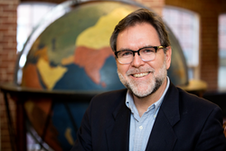 Michael Delaney pictured at Perkins School for the Blind with a tactile globe built in 1837 in the background.