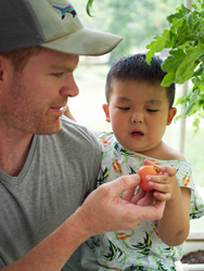 Tommy Thompson of Emergent Coils helps Ray Ray pick tomatoes in Shepherd's Field Children's Village's greenhouse