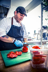 Chef storing freshly sliced tomatoes in Cambro colander food pan.