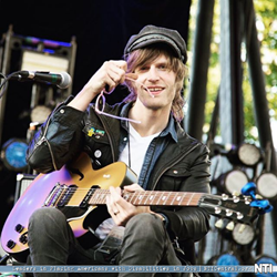 Eric Howk of Portugal. The Man posing on stage playing guitar.
