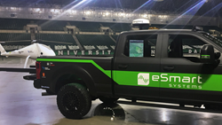 An IRIS situational awareness system is shown installed in the cab of an eSmart systems powerline inspection truck. The screen visible through the truck window plots the realtime position of a powerline inspection drone relative to the terrain.