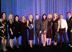 LIne of managers stand on the stage surrounding CEO who holds an award.