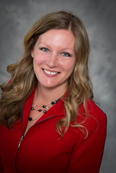Woman posing for photo wearing red top and necklace.