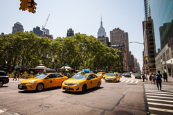 A shot of Bryant Park in NYC from the street with yellow taxis driving by. Outside Interact Marketing's NYC office location.