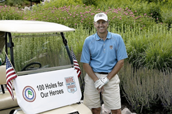 A gentleman, Carl Meyer, stands in front of a golf cart bearing a banner that reads '100 Holes for Our Heroes.'
