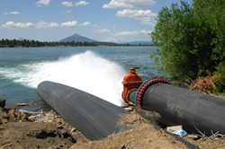 Two pipes going into a lake with one releasing water into the lake. A volcanic cone sits in the background.