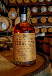 A bottle of the Tejas Ranger Creek Collaboration sitting on a barrel.