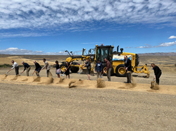Ten people turning dirt in front of a yellow grader outside at B.F. Sisk Dam.