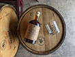 Image of the bottle and glass sitting on a barrel. The bottle is the Tejas Collaboration with Ranger Creek. Bourbon finished in a mead barrel.