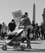 Black and white photo of two mother embracing behind an empty stroller with the Washington Monument in the distance