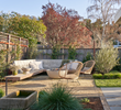 Backyard featuring a built-in l-shaped bench, modern cement firepit, extra seating, low-water plants and crunchy gravel underfoot