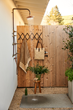 Outdoor shower built on the side of a home, featuring small wooden stool, hanging towel rack and concrete and gravel surface