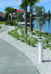 A row of white-colored, solar-powered lighting bollards line a walkway that runs near a lake