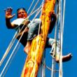 Author Allen Taube climbs up the mast on his schooner Reef Chief.