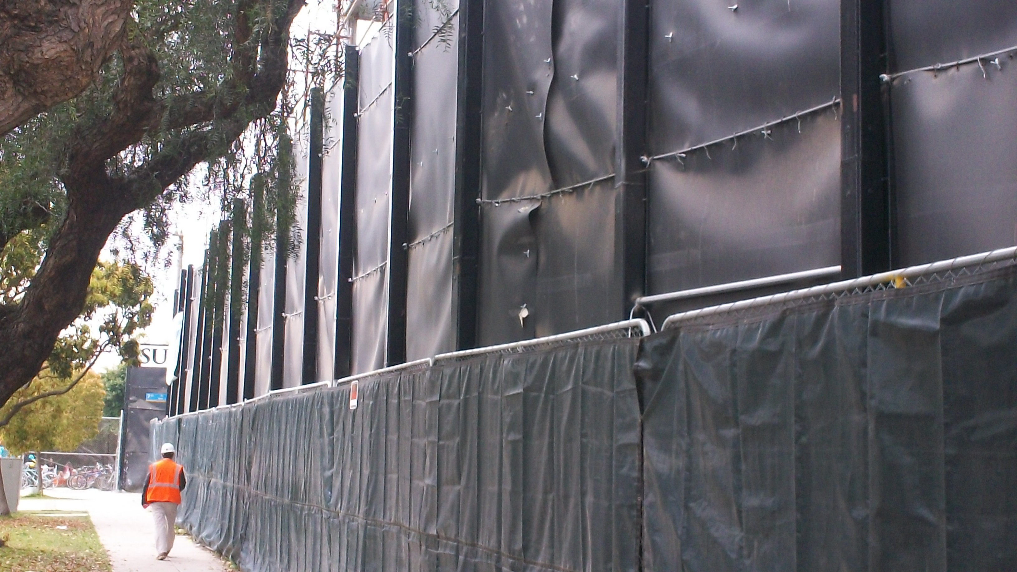 A construction worker walks on the outside portion of the 30-foot tall section of the Acoustifence barrier. The fence design utilized varying heights at different sections of the construction site.