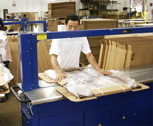 Workers protect picture frames for shipment by strapping on protective packaging.