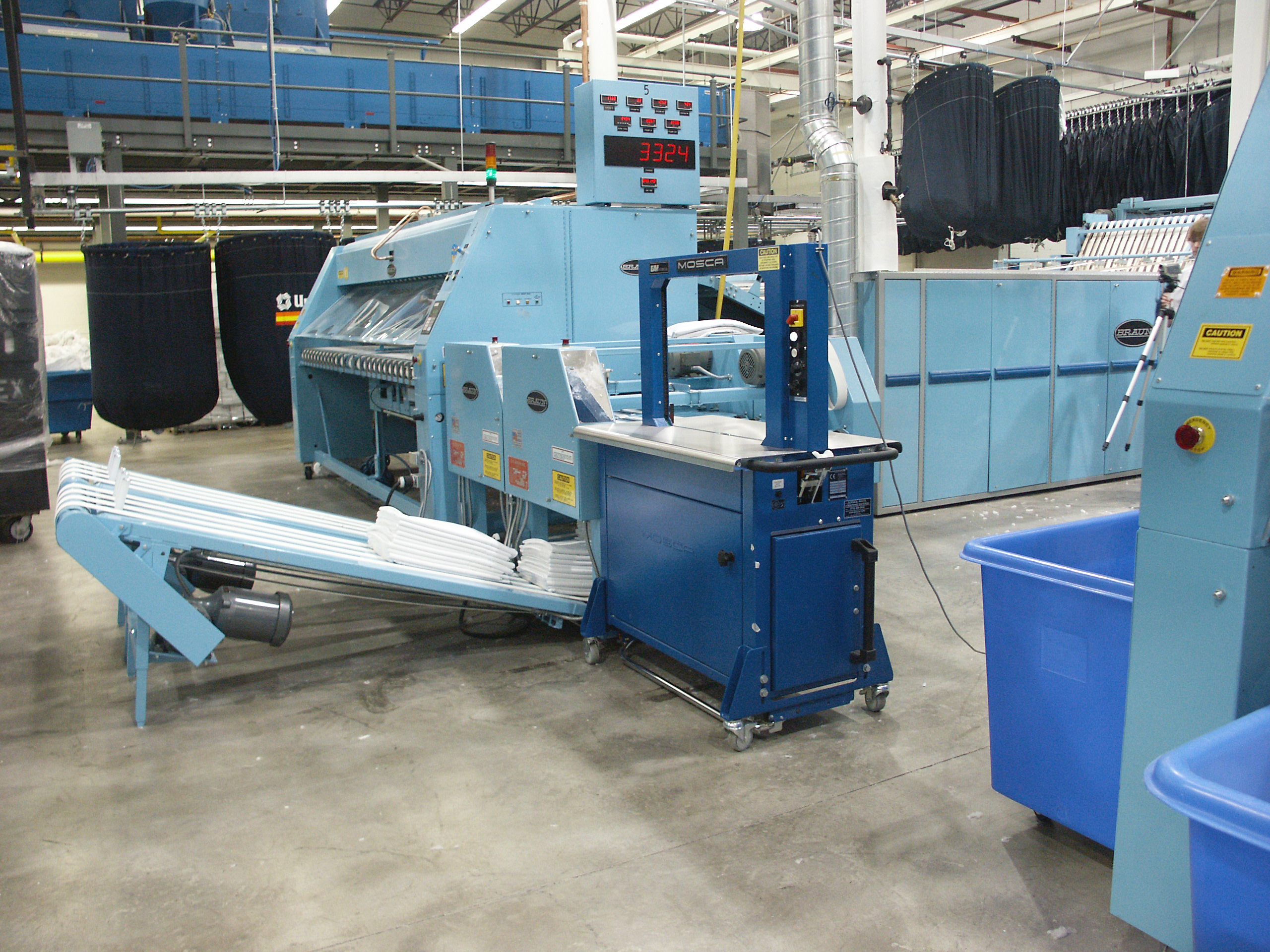 Strapping machine stands ready for bundles of textiles in large commercial laundry.