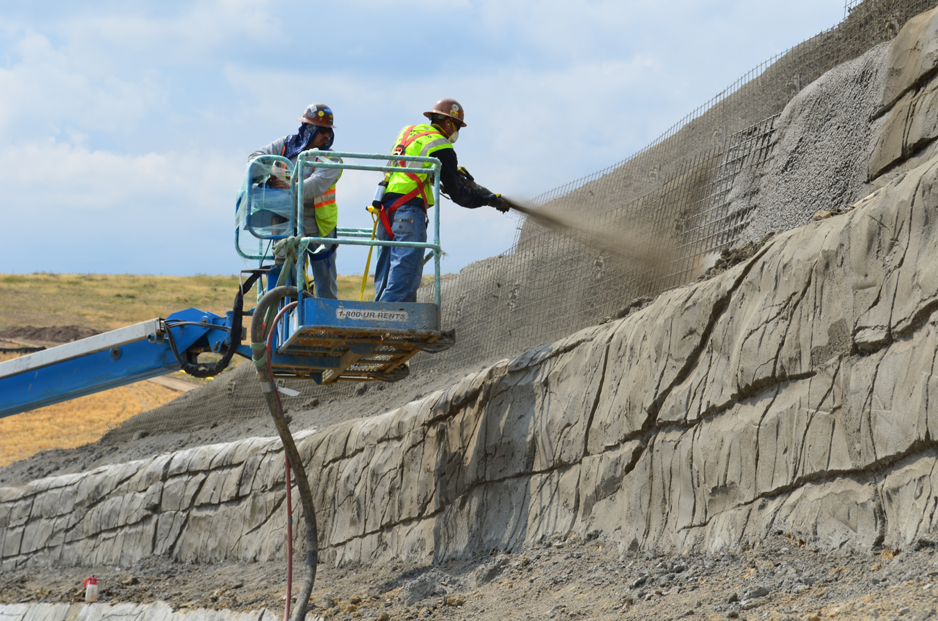 A Hayward Baker nozzleman and pump operator applying shotcrete to a soil nail lift prior to sculpting, behind a housing development in Arvada, CO.