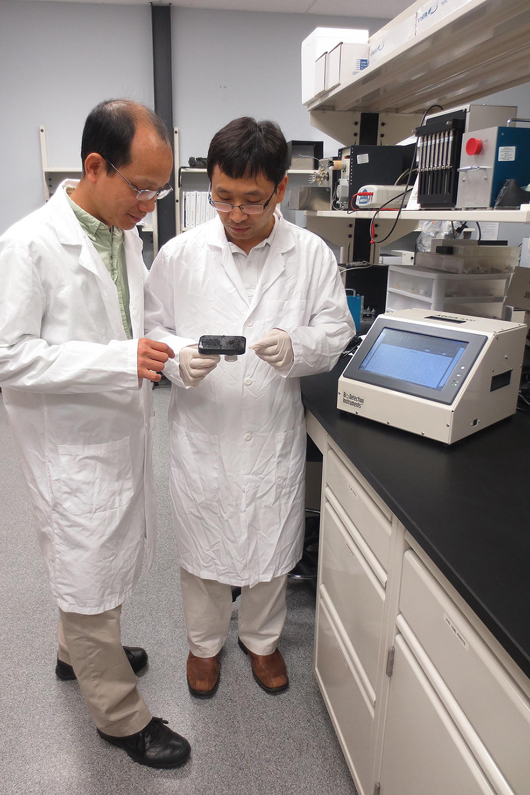 Dr. Chien Nguyen, Senior Electrical Engineer (left), and Dr. Xaioli Su, Director of Research & Development of Biodetection Instruments™, discuss the cartridge developed to detect pathogens.