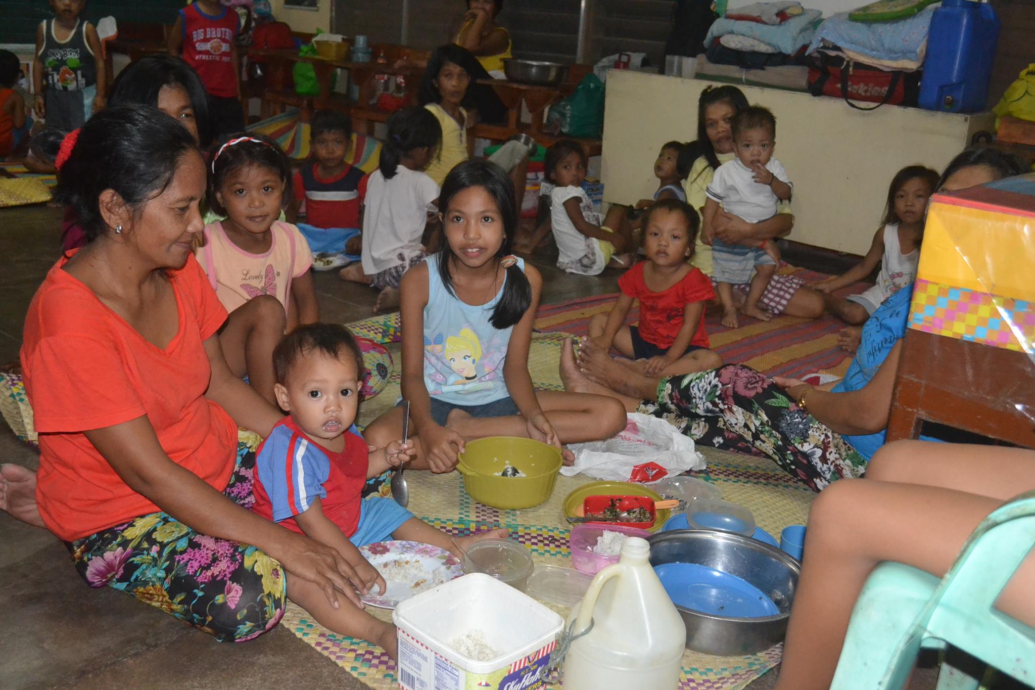 Sponsored child Kristine (center, holding a green bowl) has a meal with her family at an evacuation center.