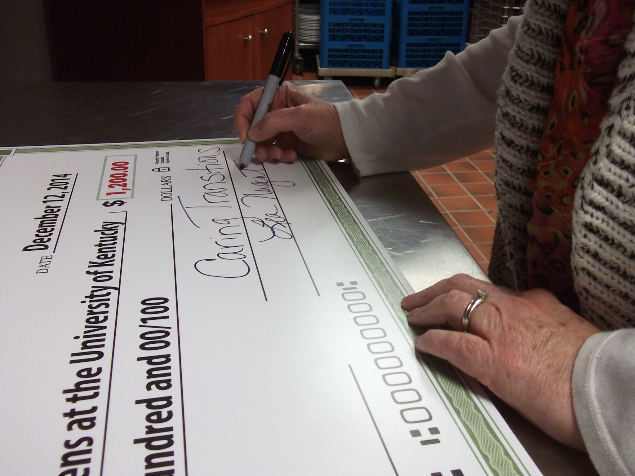 Caring Transitions Owner Lea Nugent signs the check for $1,200 donation.