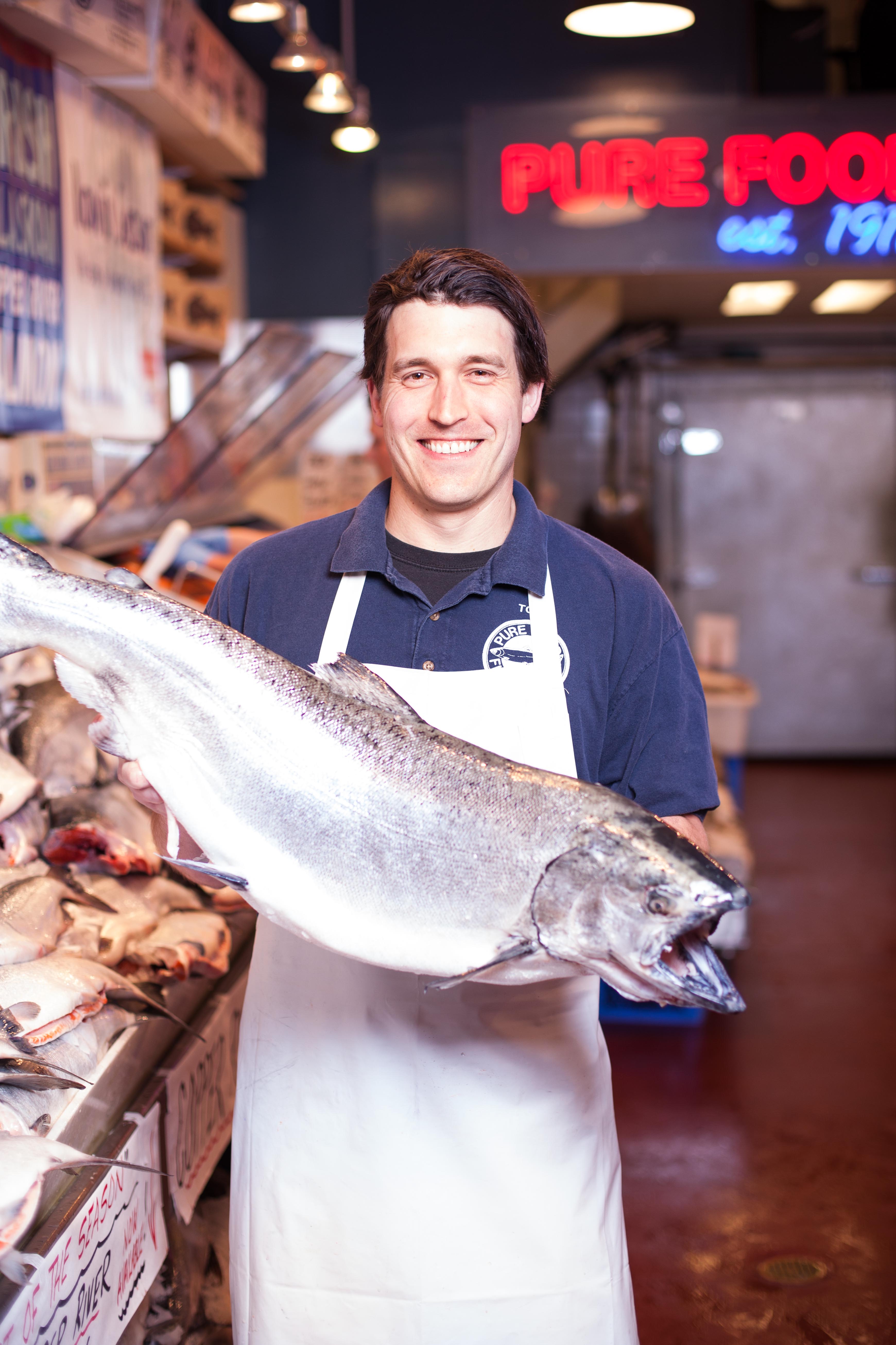 Pure Food Fish Market fish monger Tom, and a whole fresh Salmon. Photo by Jonthan Vanderweit.