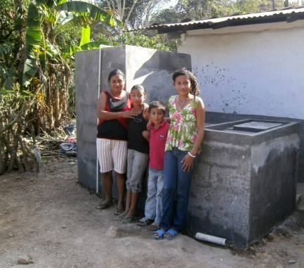 Carmen, mother of Saily, who is sponsored through Unbound, stands with her family in front of their new water tank in Honduras.