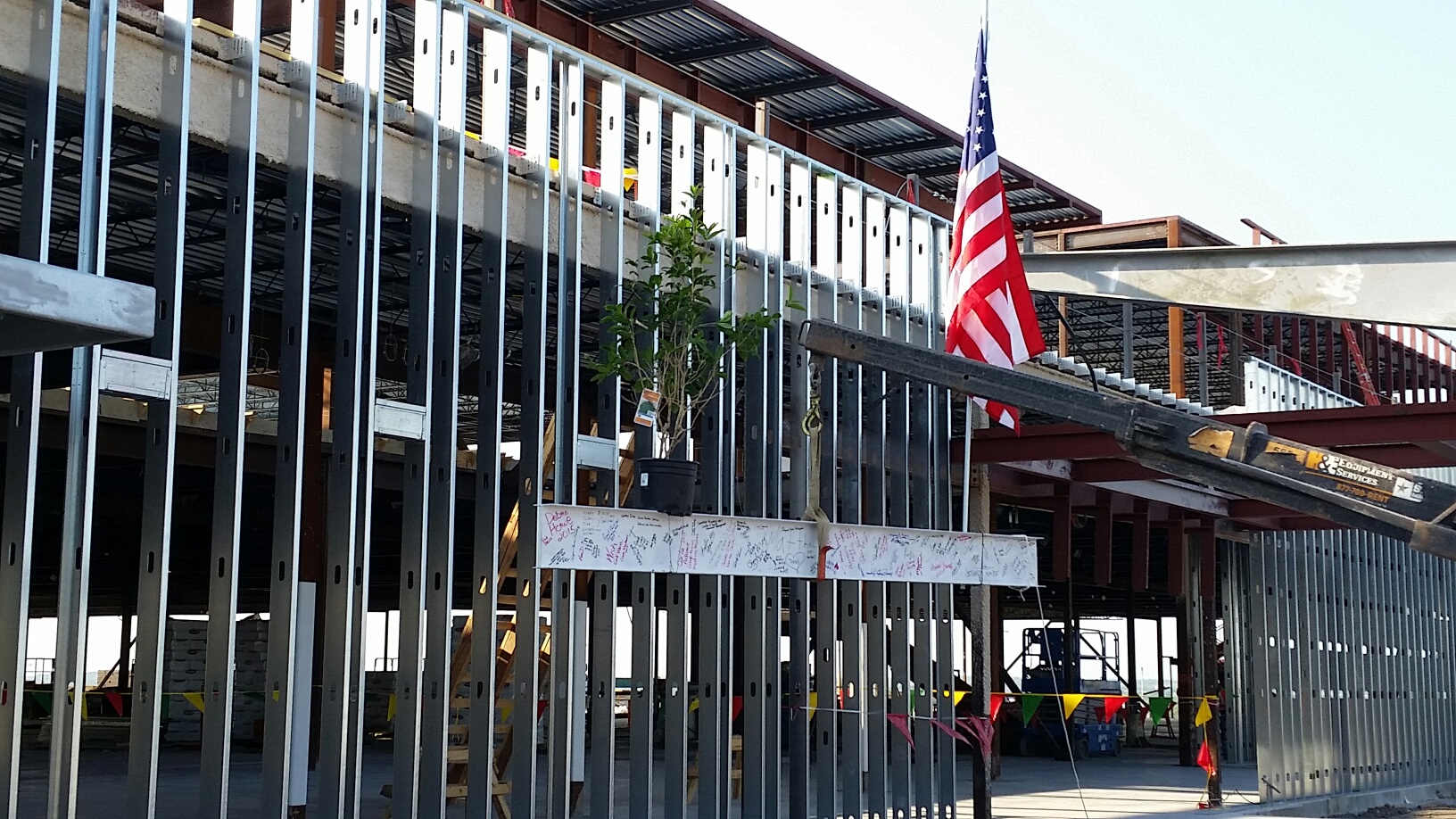 The final beam of Otto Kaiser Memorial Hospital is adorned with an American flag and an evergreen tree as it is lifted into place, signaling the building's structural completion.