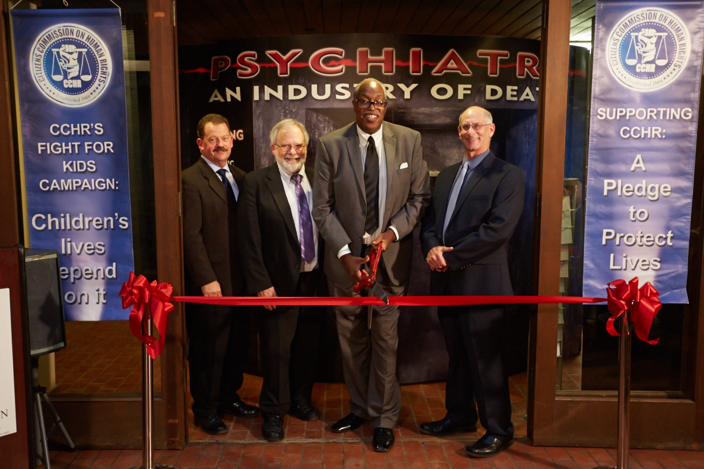 Mr. James Sweeney stands poised to cut the ribbon and officially open the Psychiatry: An Industry of Death Exhibit along with (left to right) Mike Klagenberg, Bob Johnson & Jim Van Hill.