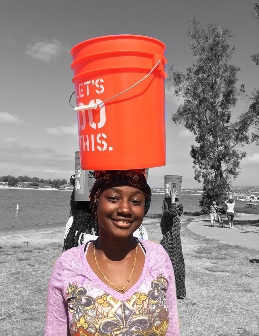 A refugee woman demonstrates how she would carry a heavy bucket of water on her head for long distances.