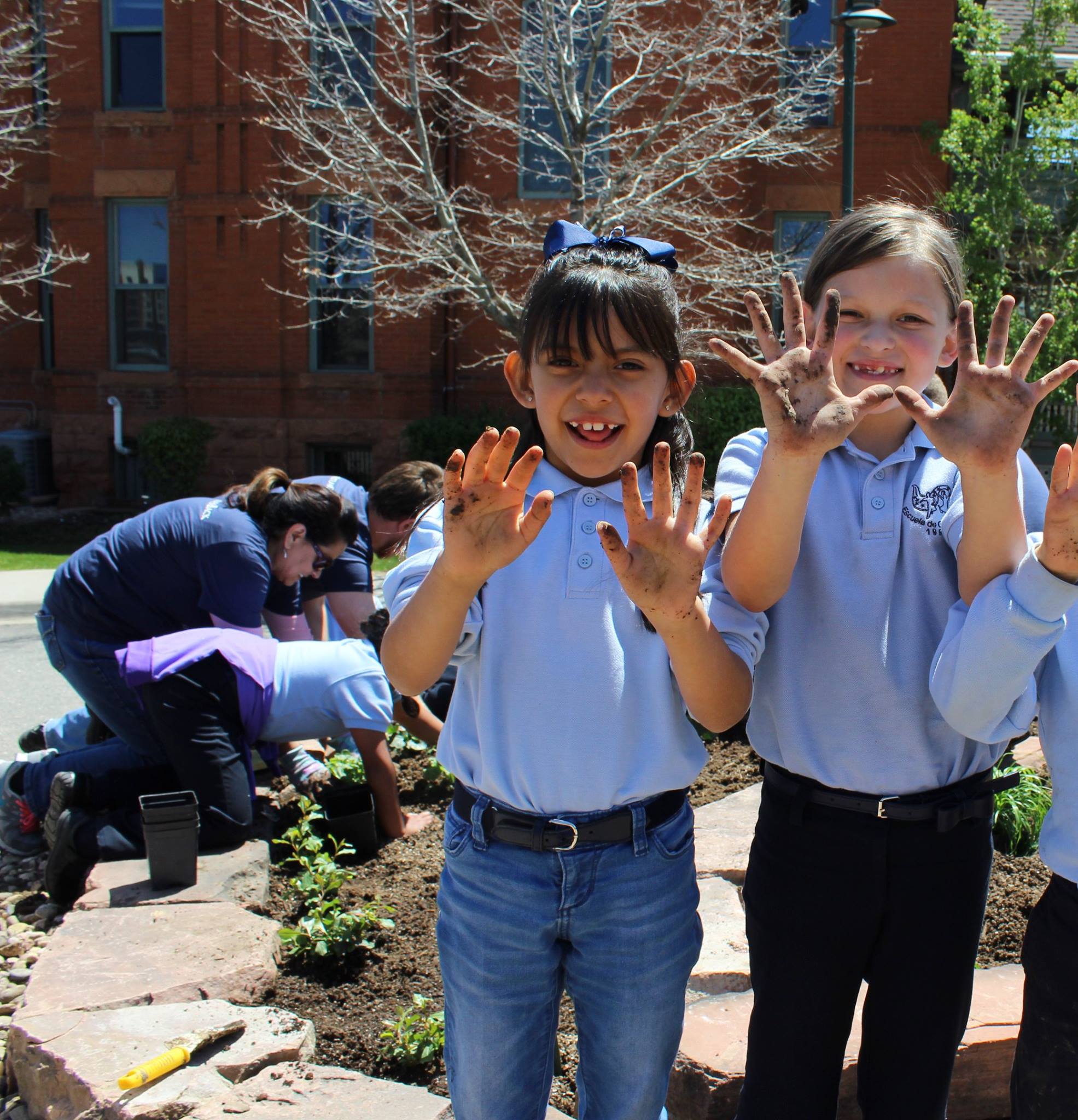 Escuela de Guadalupe students show off their dirty hands after learning to plant xeric (low water) plants with Atlas Real Estate Group team members.