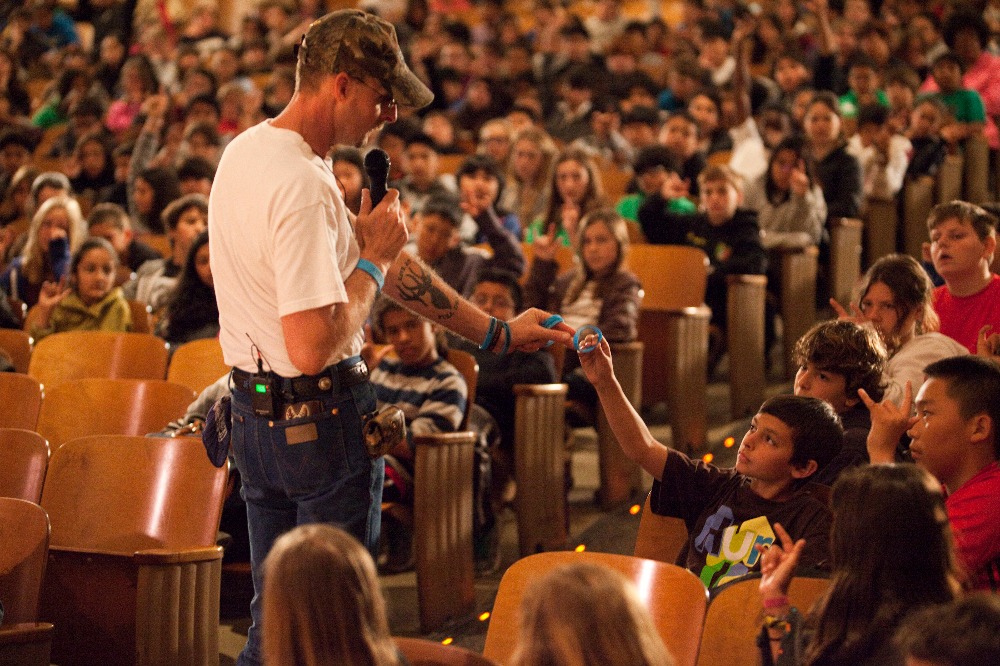 Kirk Smalley, president of Stand for the Silent, hands a wristband to a student during a recent presentation. A fundraiser started by the band The Fold aims to sponsor his presentations.