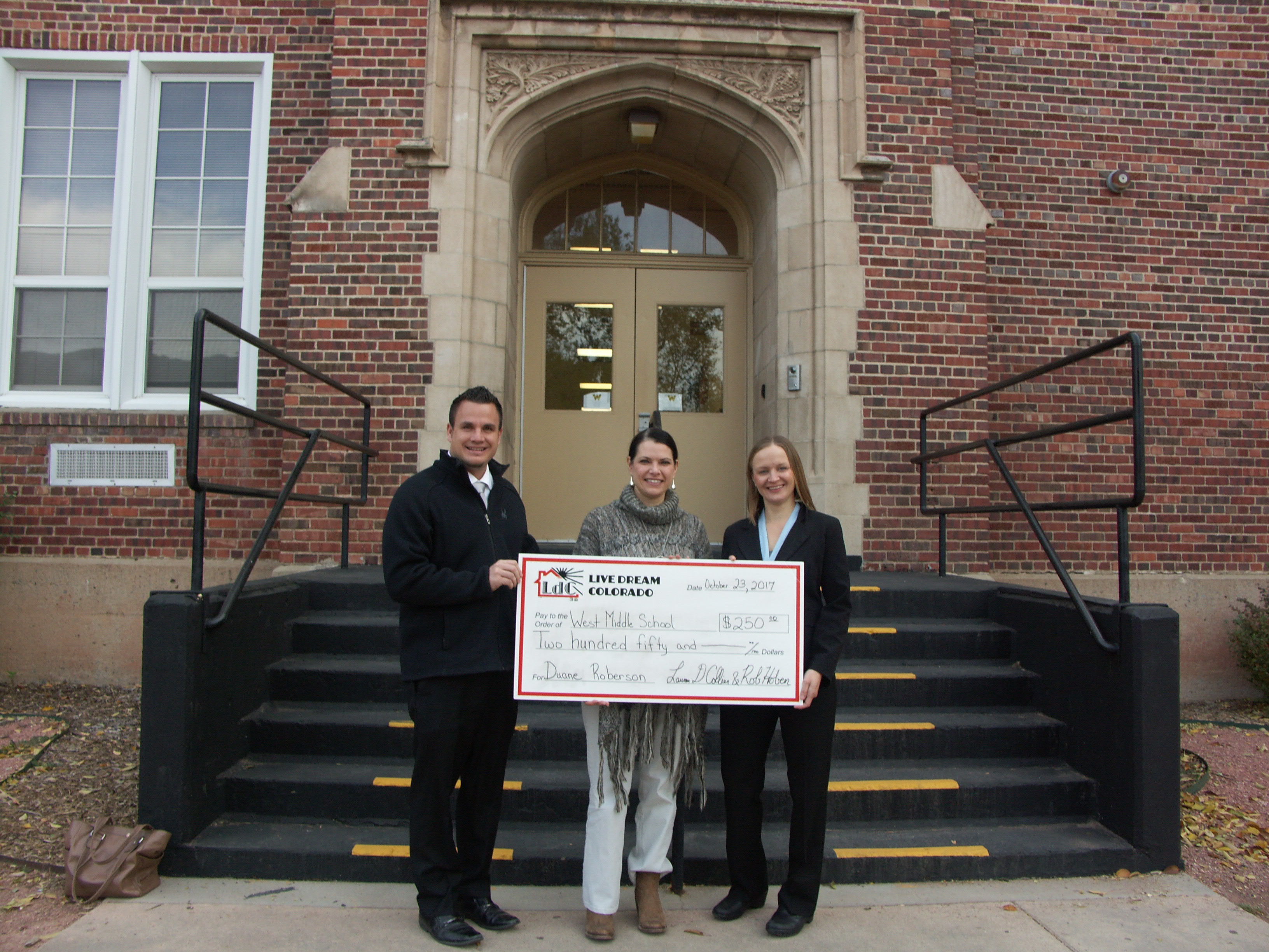 Principal Shalah Sims accepts donation to West Middle School from Live Dream Colorado in front of the school.