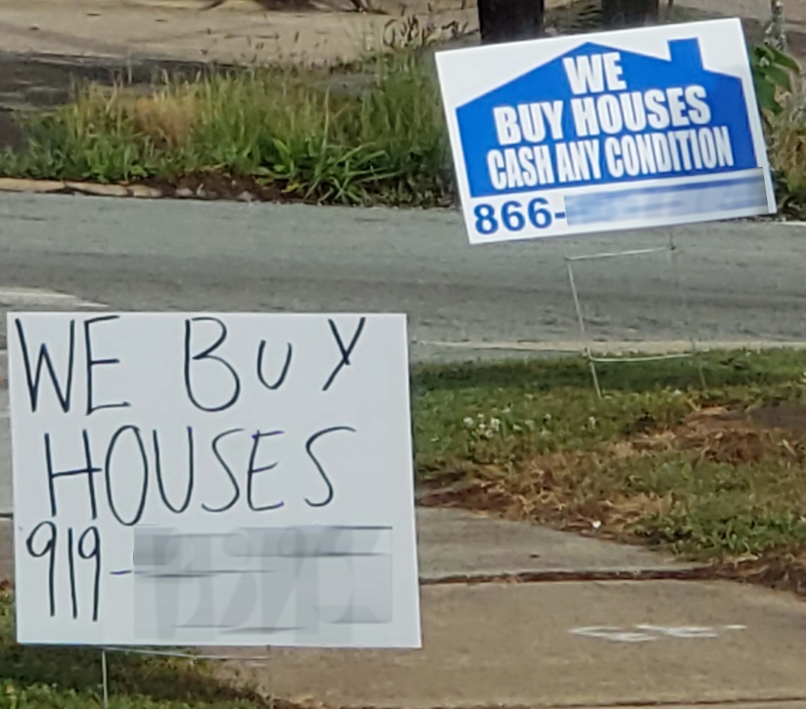 A lawn sign reads: We Buy Houses. Cash. Any condition. Another handwritten lawn sign reads: We Buy Houses.