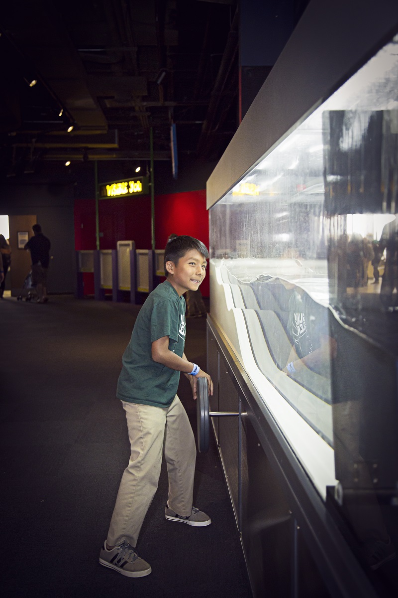 Boy explores the power of Earth's forces at the Surge of a Tsunami exhibit.