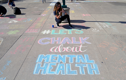 Student writes on campus sidewalk: let's chalk about mental health.