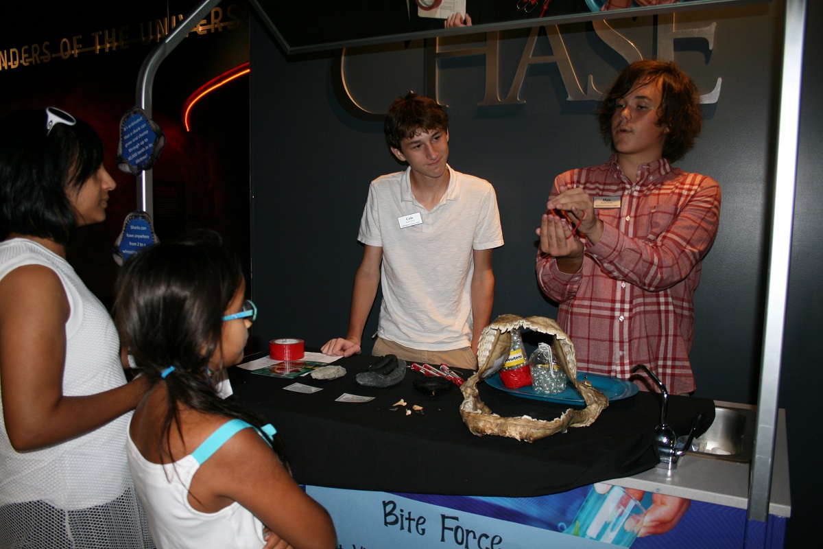 Members of Adventure Science Center's Youth CR3W help guests learn about the bite force of a shark.