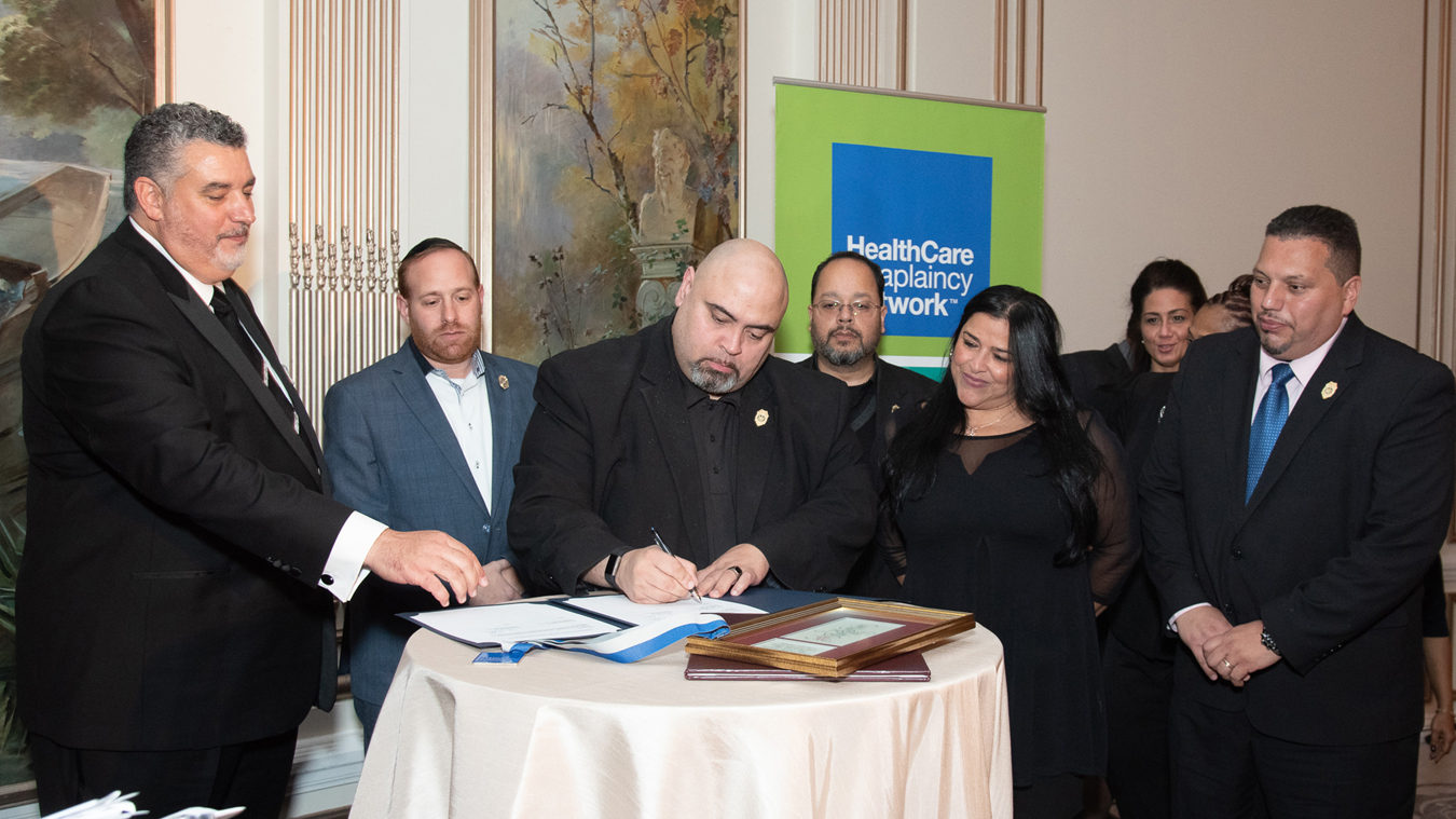 New York State Chaplain Task Force's the Rev. Marcos Miranda, center, signs documents with the Rev. Eric J. Hall, left, at HealthCare Chaplaincy Network's 2018 Wholeness of Life Gala. Photo: Ben Asen