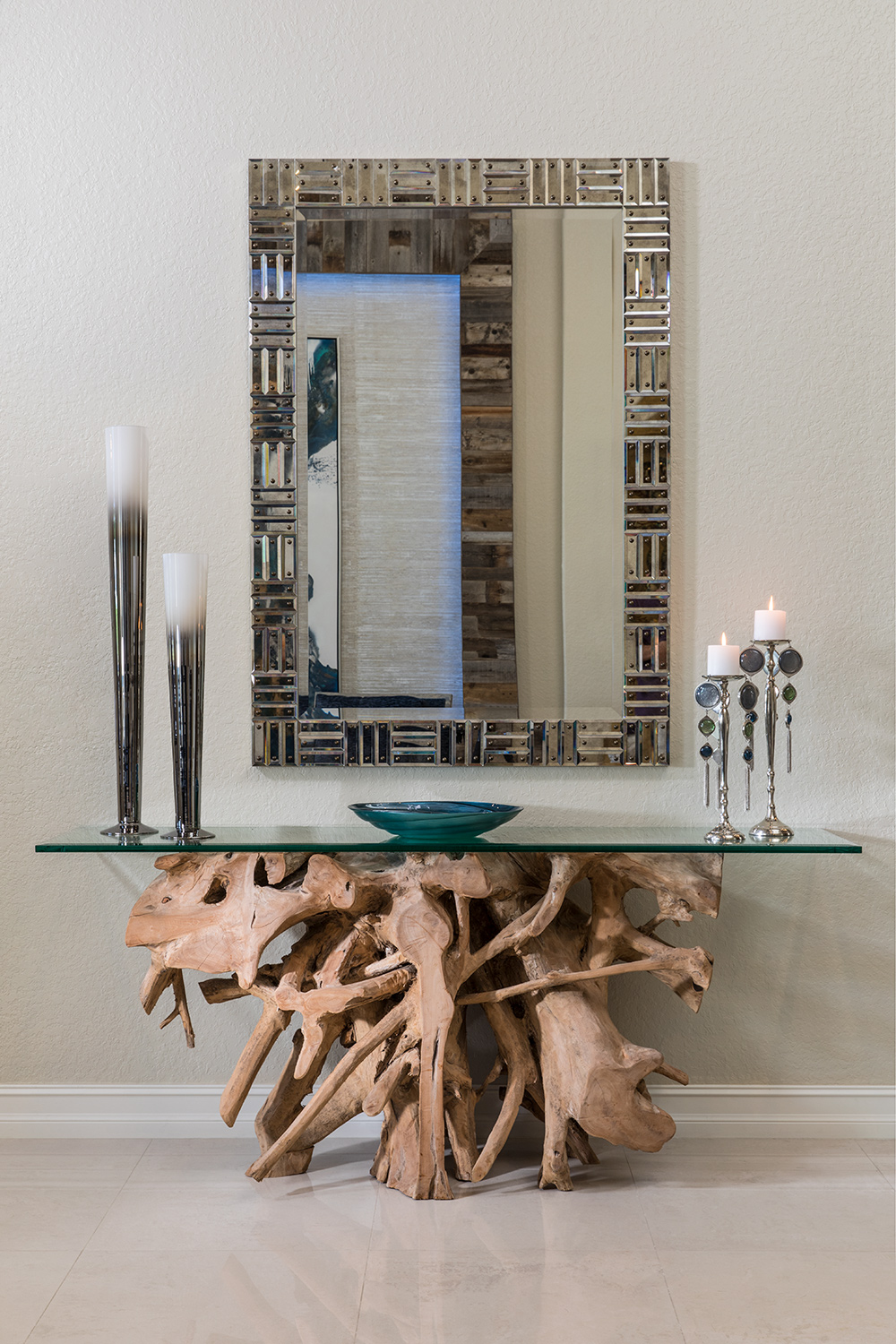 Framed mirror over glass top console table with natural driftwood base.