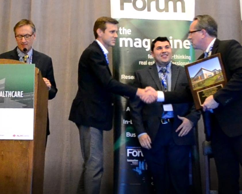 Dan Ahlering and Vlad Milrud (center) of MedProperties Group accept the 2018 award for Best MOB of less than 25,000 s.f. from HREI Editor John Mugford (left) and Publisher Murray Wolf (right).