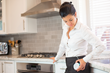 Woman standing in kitchen and checking her DFree wearable device for urinary incontinence.
