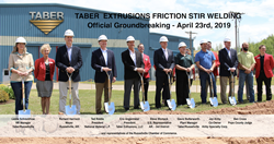 Local and State leaders pose near large open dirt piles with shovels engraved with Taber Extrusions logos on a sunny spring day at the ground-breaking ceremony for Taber Extrusions new Friction Sir Welding expansion.